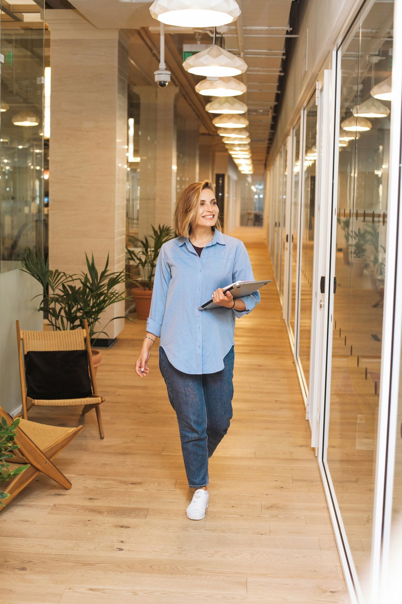 woman in blue dress shirt and blue denim jeans standing beside brown wooden chair